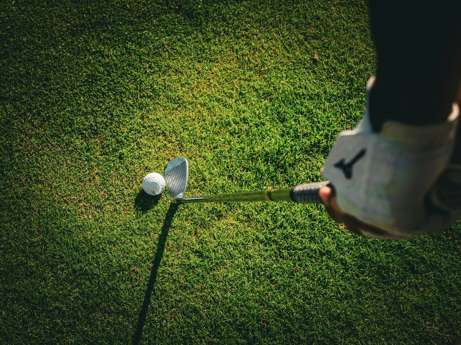 Overhead view of a golfer lining up a club behind the ball on close-cut grass