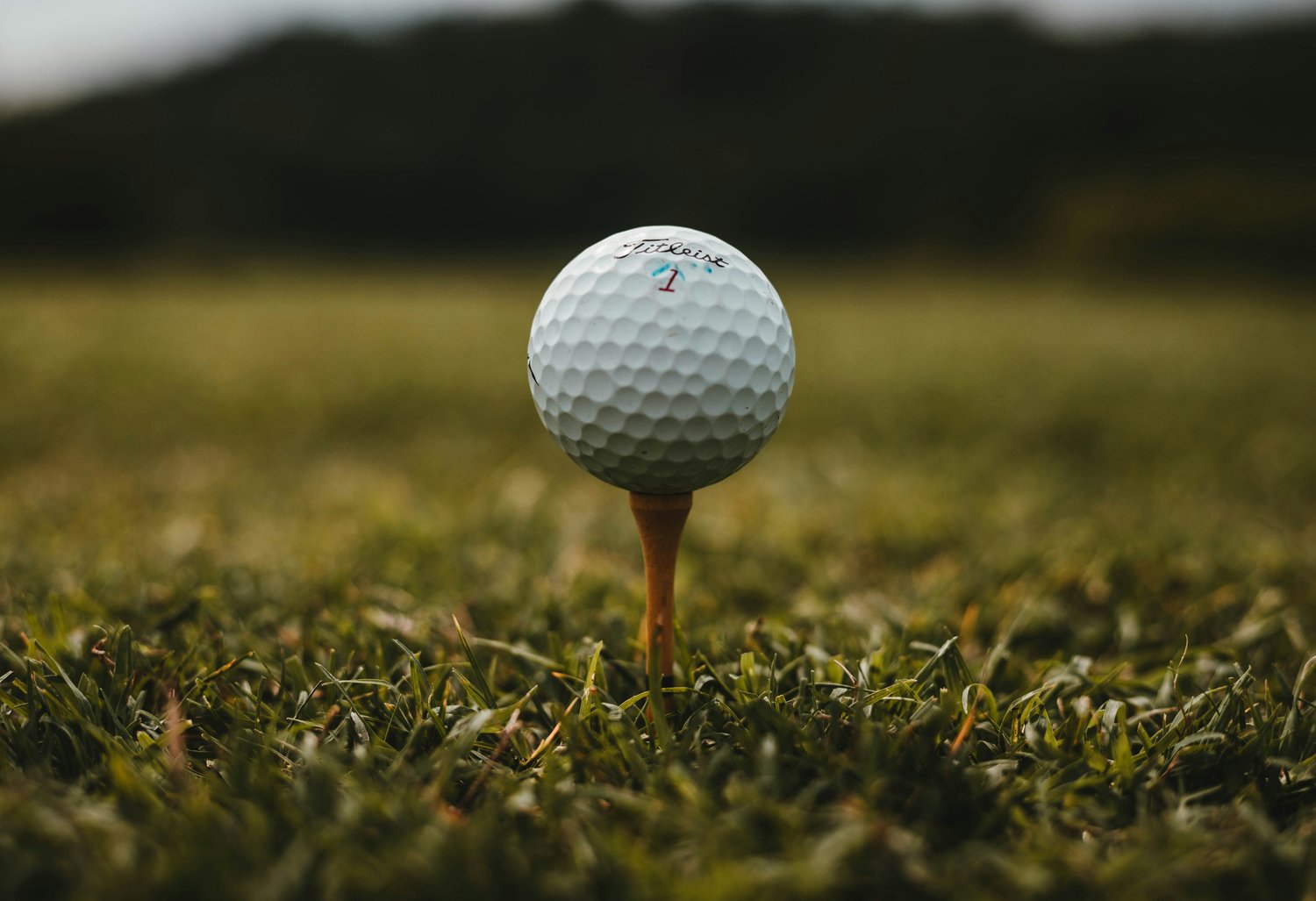 A Titleist golf ball on a wooden tee, ready to be struck, with hills behind